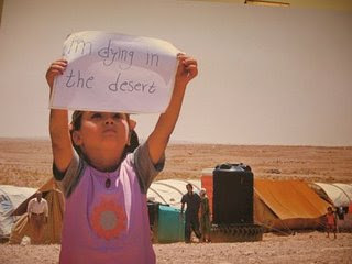 A Palestinian Iraqi child holds up a sign saying 'I'm dying in the desert' in the Al-Tanf refugee camp.