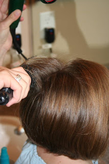 Side view of young girl's hair being styled with a blow dryer and round brush