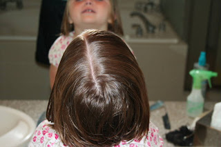 Back view of young girl's hair being styled into "Two Messy Twists on Top" Hairstyle