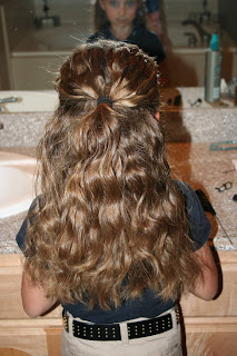 Back view of young girl's hair being styled into "Curls After Triple Twists w/ Messy Buns" hairstyle