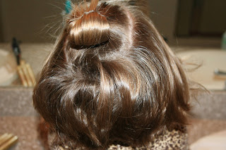 back view of young girl's hair being styled into 3-barrel curl hairstyle on her a-line bob