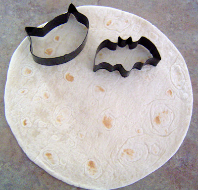 a flour tortilla with a bat and cat shaped cookie cutter sitting on top of it