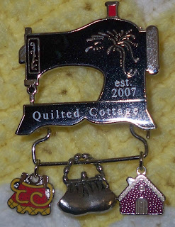 Quilted Cottage pin which is a sewing mach8ine with three charms attached to a bar beneath the machine