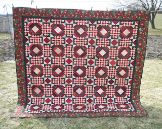 Red and green Carolina Crossroads quilt hanging on the clothesline in the backyard