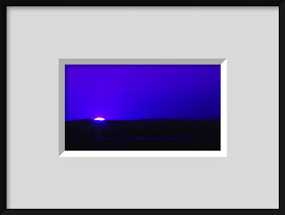 A framed photo of a glowing blue moonrise is an abstract explosion of color with a silhouette of the horizon.