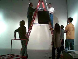 Gallery test installation, box poised near top of stepladder.