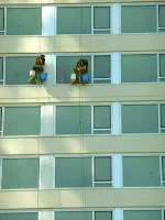 Dos lavadores de vidrios de ventanas en altura en edificio de departamentos.