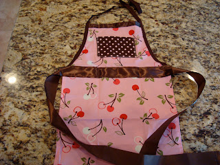 Little girls apron that is pink, brown and has cherries