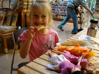 Young girl eating pita chip at table full of barbies