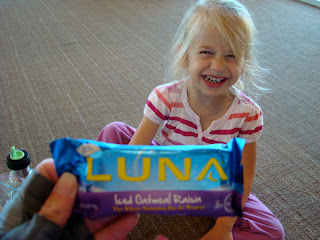 Hand holding Luna Bar with young girl smiling in background
