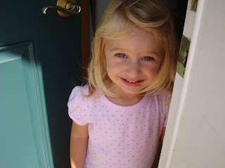 Little girl with door ajar smiling in pink shirt