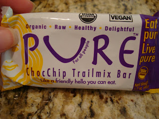 Hand holding Pure ChocChip Trailmix Bar in package