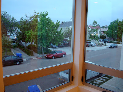 View out living room window of houses, trees and cars