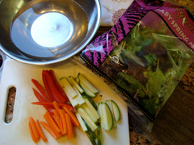 Sliced vegetables, bowl of water and bag of baby spring mix