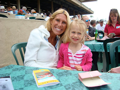 Young girl sitting on woman's lap at table at racetrack