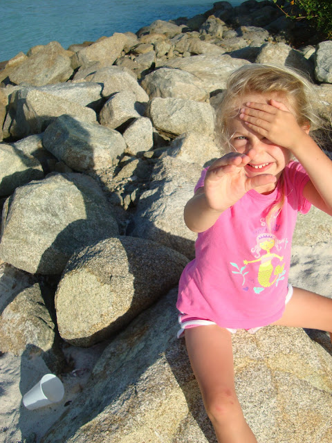 Young girl on rock shielding eyes from sun and reaching out