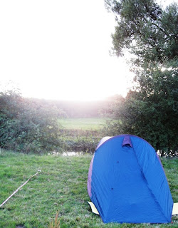 Tent on riverbank with sun setting