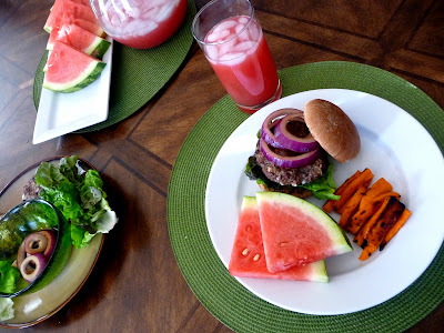 A blue cheese burger on a white plate with watermelon slices and sweet potato fries. 