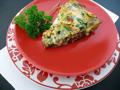 A slice of Italian sausage frittata on a red plate with a piece of parsley. 