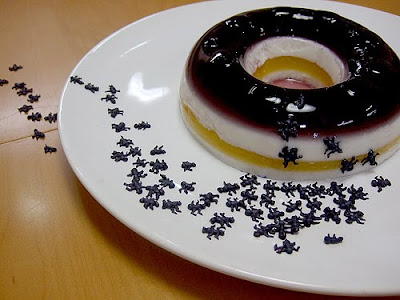 A donut shaped jello layered desert on a plate with fake ants on top and leading off of the plate. 