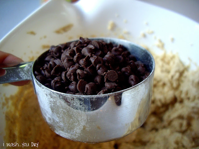 A measuring cup of chocolate chips above a bowl of cookie mix. 