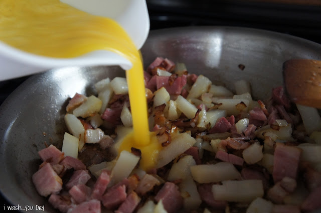 Eggs being poured into a skillet with chopped potatoes and ham.