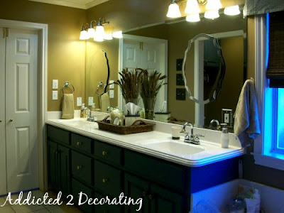Master bathroom makeover--oak cabinets were painted blue, decorative mirrors hung over plate glass mirror, new lights, and decorative accessories