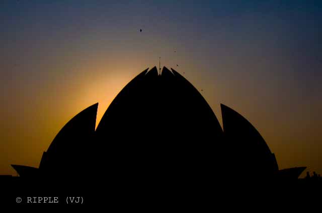 Sunset View @ Lotus Temple, Nehru Place, Delhi: The Baha'i House of Worship in Delhi which is popularly known as the Lotus Temple due to its flower like shape, is a Bahai House of Worship and also a prominent attraction in Delhi. It was completed in 1986 and serves as the Mother Temple of the Indian subcontinent. It has won numerous architectural awards and been featured in hundreds of newspaper and magazine articles.: Posted by Ripple (VJ) on PHOTO JOURNEY @ www.travellingcamera.com : ripple, Vijay Kumar Sharma, ripple4photography, Frozen Moments, photographs, Photography, ripple (VJ), VJ, Ripple (VJ) Photography, Capture Present for Future, Freeze Present for Future, ripple (VJ) Photographs , VJ Photographs, Ripple (VJ) Photography : Again a silhouette of Lotus Temple but colors on the back are not so good... This shows the dullness of poluted sky in Delhi :-(The temple is shaped in the form of a half opened Lotus Flower and the main structure encircled by nine ponds. There are nine doors that lead to the central hall. Number nine is considered sacred in Bahai faith which depicts all the major nine faiths of the World. The central hall suggests that all nine religions are dedicated to the sole God. This central hall can manage 2500 people at a time.