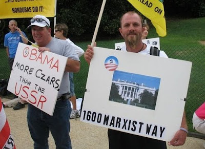 idiot teabaggers with signs that say Obama: More Czars Than the USSR and 1600 Marxist Way under a picture of the White House