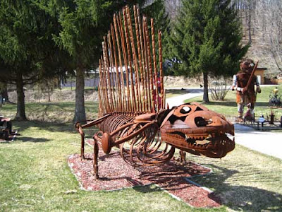 Rusted steel sculpture of a four-legged dinosaur with vertical bars along its spine