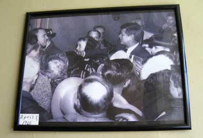 Black and white photo of John F. Kennedy shaking hands in a crowd of people