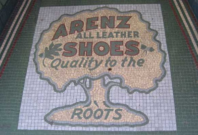 Old tile mosaic of a tree. Words say Arenz all leather shoes, Qualit to the roots