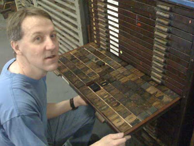 Greg Corrigan kneels by a drawer of unusual wood type