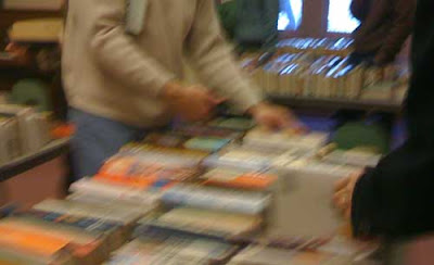 Blurry photo of a ban bending over a table full of books with an electronic device in his hand