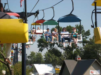 People sitting in multi-colored ski-lift chairs as they ride over the Fair