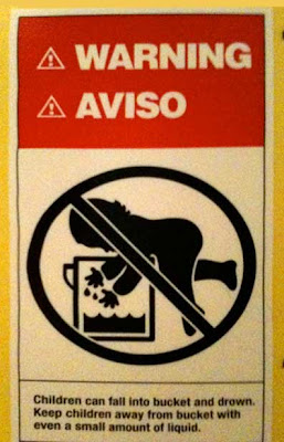 Red, white and black warning label showing a toddler falling into a bucket with some water at the bottom