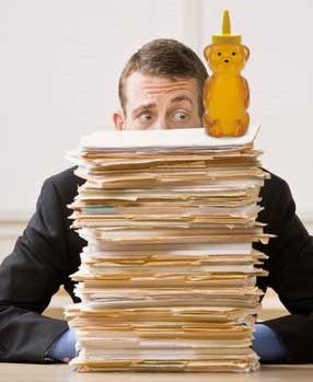 Surprised looking man with a huge pile of file folders in front of him. Atop the pile is a plastic bear bottle full of honey.