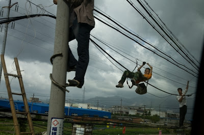 Men repairing power lines by hanging off of them using a sling