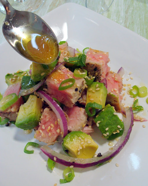 Spooning the dressing over the top of the tuna avocado salad on a dish. 