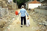 An elderly Chinese woman with bound feet walks through the rubble of demolished homes in a 'hutong' or lane. 