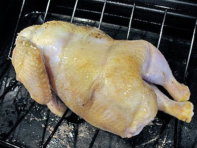 A close up photo of a whole chicken on a roasting pan.