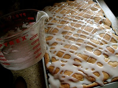 A close up photo of glaze being poured over a pan of blackberry pie squares.