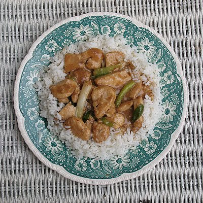 An overhead photo of chicken scallion stir fry over white rice on a teal and white plate.