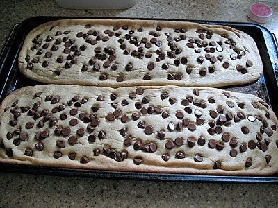 Freshly baked cookie stick dough spread in two long portions onto a baking sheet with chocolate chips on top.