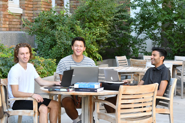 Three students sit at an outdoor table.