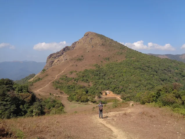 hiker gauges the the mightiness of the kabbe hills the twin sister of the tadiandamol peak of coorg